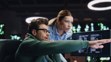 Karanlık sunucu odasında birlikte çalışan programcı çift. Bilgisayar uzmanı kadın patrona analitik verileri gösteriyor. Siber güvenlik konularını tartışan iki veri tabanı analisti