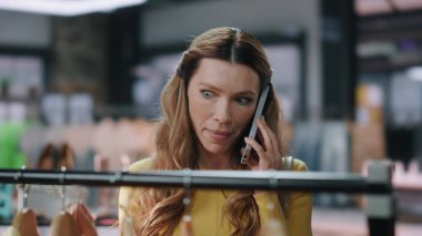 Giyim mağazasında konuşan bayanı aramak fiyatları şok etti. Kadın müşteri elbiseleri butikte akıllı telefon görüşmesinde pahalı şeyleri tartışıyor. Gergin alışverişkolik elbise seç