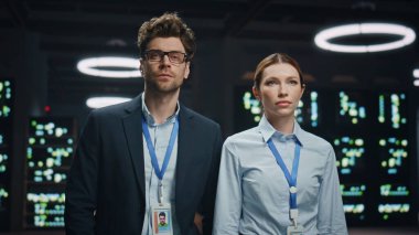 Modüler veri tabanında poz veren ciddi teknisyen çifti. Bilgi işlem yöneticileri iş arkadaşları ağ depolama sunucu odasında kameraya bakıyor. Modern kabinedeki mühendis meslektaşları 