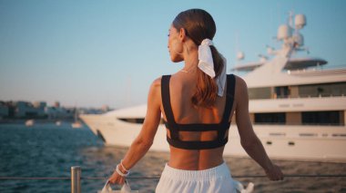 İskelede, demirli beyaz yatıyla bronzlaşmış bir kadın poz veriyor. Arka manzara muhteşem kız güneşli zeminde durup tatilin tadını çıkarıyor. Zarif, çekici, sevimli gülüşlü kamera..