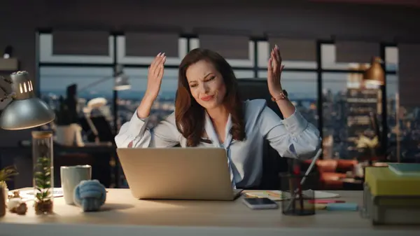Upset lady reacting fail at night city view workplace. Disappointed woman feeling displeased working on laptop at modern office. Mad loser gesturing hands having work business problems at cabinet