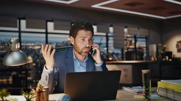 Worried ceo calling phone sitting at city view window dark office closeup. Confident bearded executive manager have serious telephone conversation feeling stress. Nervous business man smartphone talk