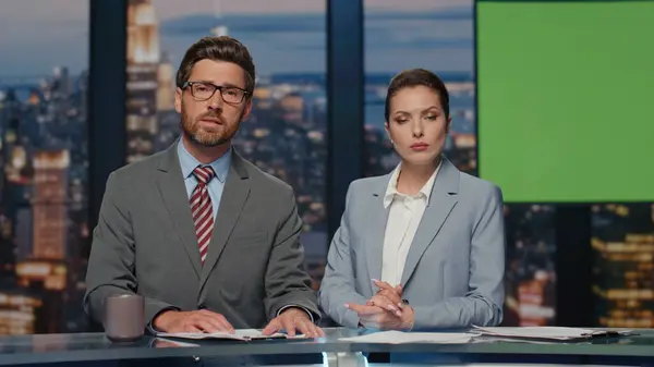 stock image Serious news readers broadcasting chroma key tv newscast in night studio closeup. Positive charismatic presenters communicating with audience ending daily reportage. Anchorwoman winking to camera