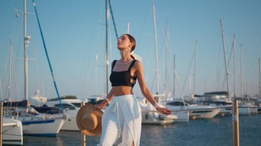 İskelede poz veren sakin kadın yaz rüzgarının tadını çıkarıyor. Muhteşem lüks bir model, beyaz yatların önünde duruyor tatilde dinleniyor. Zarif kız gözlerini kapatıp iskelede yüzünü güneş ışığına çıkarıyor..