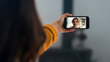 İki arkadaş video kaset kapanışı hakkında konuşuyor. Kız elleri evde cep telefonu ekranı tutarak el kol hareketi yapıyor. Bilinmeyen kadın konferans uygulaması kullanarak çevrimiçi sohbetten hoşlanıyor. Sanal çağrıdaki uzak meslektaşlar