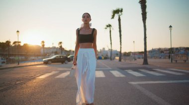 Günbatımında şık kıyafetlerle yürüyen zengin bir iş kadını. Yaz akşamında asfalt yolda kendine güvenen esmer kadın. Modayı takip eden başarılı bayan güzel günbatımının tadını çıkarıyor..