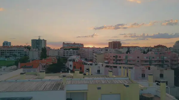 Calm urban sunset drone view over cozy residential buildings. Golden sun setting over sky horizon with light clouds. Picturesque sundown at evening cityscape aerial shot. Beautiful mediterranean town.