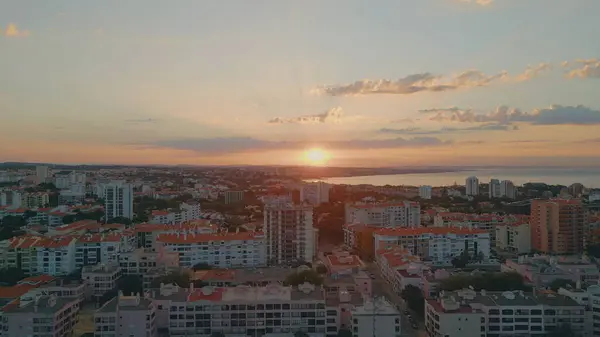 Golden sundown over coastal city drone view. Bright evening sun shining on beautiful mediterranean town. Picturesque urban sunrise at waterfront aerial shot. Orange morning skyline with light clouds.