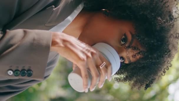 快乐的女人在城市公园里喝着外卖咖啡 迷人的非洲裔美国女商人穿着时髦西服 带着笑着垂直拍摄的相机 在户外享受饮料的异性恋女孩 — 图库视频影像