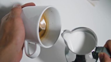 Bilinmeyen barista sürahiden sütlü kahve dolduruyor. Erkek eli, aromatik içeceğe kremalı sıvı ekleyerek leziz, dikey latte odaklı yapar. Cappuccino hazırlama işlemi.