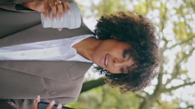 Konuşan bir kadın şehir parkında yürürken çekilmiş video görüntüsü. Elinde kağıt kahve fincanı var. Çekici özgüvenli Afro-Amerikan iş kadını açık havada konuşuyor. Kız akıllı telefon kamerası dikey görünümü kullan.