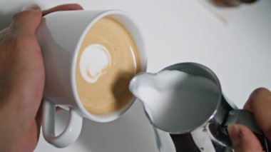 Erkek elleri kahve dükkanında latte yapıyor. Yakından. Bilinmeyen baristanın aromatik kahveye krem şanti dökmesi mükemmel bir cappuccino dikey çekimi yaratıyor. Kafe çalışanı, nefis içeceklere kalbinin sesini dinletiyor.