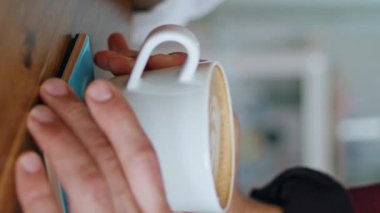 Barista 'nın elleri, akıllı telefonları kapalı oturan kadın müşteriye kahve servisi yapıyor. Bilinmeyen garson Afro-Amerikan kız dikey videosuna latte getiriyor. Genç bayan beyaz kupayı alıyor.