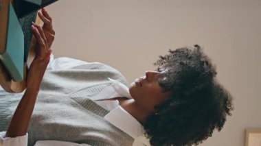 Afrika kökenli Amerikalı bir kız güzel bir ev ofisinde çalışıyor. Kendine güvenen kıvırcık kadın modern laptop dikey görüntüsünde internette sohbet ediyor. İş için internet teknolojisini kullanan çekici stil sahibi bir bayan.