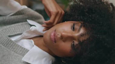 Güzel bir kafede bekleyen bir kadın. Yakın çekim. Şehvetli, rahat, Afro-Amerikalı bir kızın portresi. Restoran masasında tek başına oturuyor. Mutlu kıvırcık kadın kamerayı dikey gülümsemeyle görüyor.