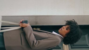 İş kadını siyah kapıyı kapatarak evi terk ediyor. Afro-Amerikalı kendine güvenen bir bayan modern akıllı telefonu dikey olarak tutuyor. Ciddi kıvırcık kız takım elbise giyerek buluşmaya gidiyor.