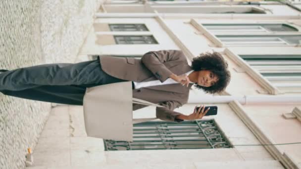 女孩使用智能手机自费站在街上 年轻自信的非洲裔美国女人在屏幕上拍摄户外垂直录像 迷人的 轻松的 带着现代电话步行的女士 — 图库视频影像