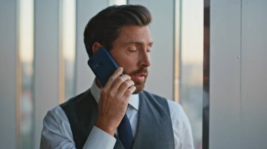 Portre kendinden emin lider panoramik ofis vitrininde cep telefonuyla konuşuyor. Yakışıklı bir danışman iş problemleri hakkında pazarlık yapıyor. Başarılı orta yaşlı bankacı iş adamı konuşuyor. 