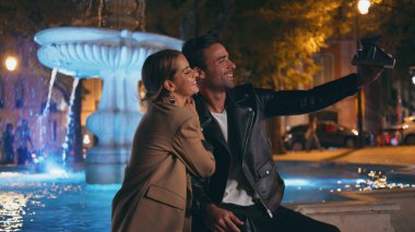 Sevgili çift akşam şehrinde fotoğraf makinesiyle fotoğraf çekiyor. Mutlu aşıklar randevularında fıskiyede selfie çekerken eğleniyorlar. Mutlu evli insanlar tatil gezisinde fotoğraflara bakarlar..