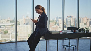 Kadın profesyonel daktilo masasında cep telefonu. Başarılı finans yöneticisi panoramik ofiste akıllı telefon kullanarak e-posta göndermeyi kontrol etti. Şık kadın şirket lideri iş yerinde internette dinleniyor..