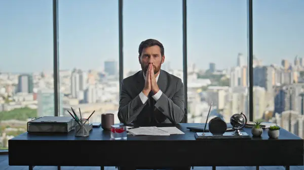 Corporate businessman thinking decision at cityscape closeup. Serious man in suit looking camera pondering problem in glass office. Worried financial manager posing at desk. Crisis bankruptcy concept
