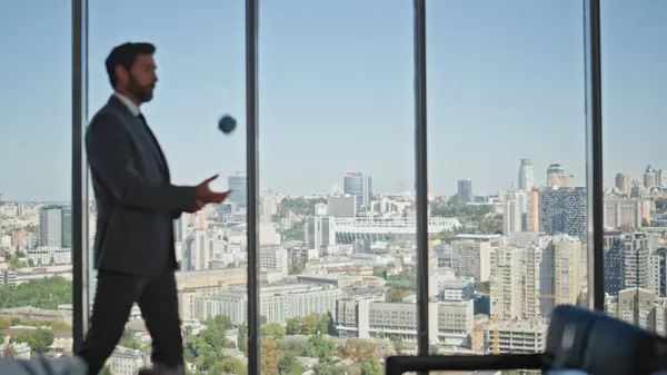 Worried businessman walking office room at panoramic widow. Man silhouette in suit throwing ball thinking company future at cityscape view. Corporate manager executive resting waiting partners meeting