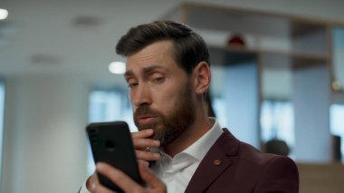 Üzgün liderin cep telefonuyla konuşması ofiste can sıkıcı bir video görüşmesi. Yakın plan iş adamı hayal kırıklığına uğramış akıllı telefona bakıyor. Yorgun yönetici çevrimiçi konuşma yapıyor. CEO sorunları tartışıyor