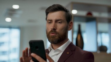 Ofisteki videolu iş adamının cep telefonu. Kendine güveni tam bir yönetici iş ortağıyla görüntülü konuşma yapıyor. Akıllı telefonu tek başına kullanıyor. Ciddi bir yönetici iş yerinde çevrimiçi konferans düzenliyor.