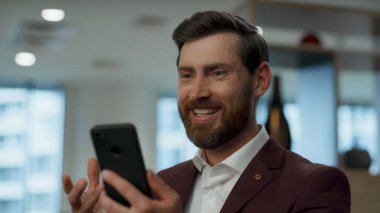 Akıllı telefondan konuşan mutlu bir işçi. Yakın plan. Memnun ofis çalışanı cep telefonundan iyi haberler alırken gülümsüyor. Başarılı bir şirkette videodaki olumlu kahkaha konuşmaları. Patron başarının tadını çıkar