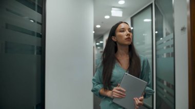 İş merkezinde gülen kasıtlı çalışan selamı. Esmer iş kadını ofis koridorunda tablet bilgisayar tutuyor. Lüks açık alan koridorunda buluşmak için heyecanlı bir profesyonel koşuşturma 