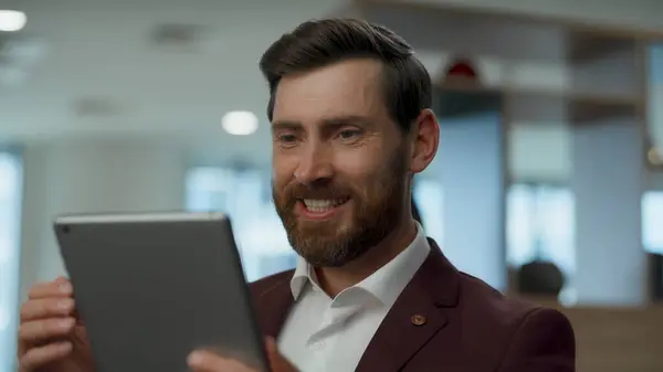 Excited man receiving message at modern lobby closeup. Bearded director reading good news on tablet computer screen at lounge. Happy person making winning gesture alone. Happy coworker success