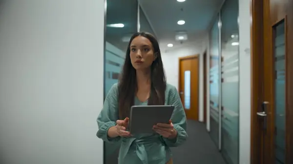 Woman ceo searching tablet computer in office. Busy manager walking through corridor in modern workplace. Business person looking corporate data in glass wall hallway. Professional diverse concept