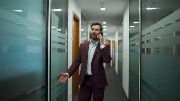 Smiling boss having mobile conversation indoors. Closeup happy project manager talking discussing cellphone in modern office building corridor. Skilful man using phone in coworking luxury workplace