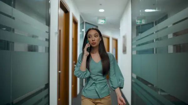Smiling boss having mobile conversation indoors. Closeup happy manager talking discussing cellphone in modern office building. Joyful woman using phone going corridor in coworking luxury workplace