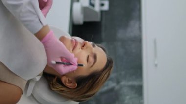 Profesyonel güzellik uzmanı, kadın yüzüne dikey beyaz kalemle düzeltme çizgileri çiziyor. Prosedürü gençleştirme konusunda uzman. Estetik kozmetik uzmanı cilt üzerindeki sorun bölgelerini işaretliyor
