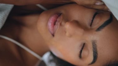 Otelde rahat uyuyan kadın yastığı. Kıvırcık saçlı tembel kız yatak odasındaki portreye bakıyor. Afro-amerikan modeller sabah dikey çekimde kestiriyorlar. Sakin bayan uyandı.