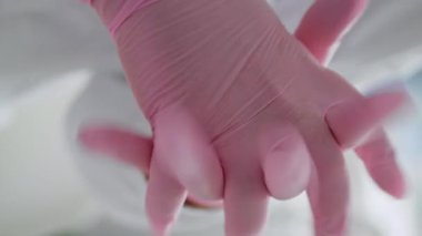Doktor elleri pembe lastik eldivenler takıyor. Dikey odaklı, yakından. Klinikte sterilite hijyeni önemseyen tanınmamış bir kadın doktor kozmetolojisti. Sağlık çalışanı muayene prosedürlerini hazırlıyor.