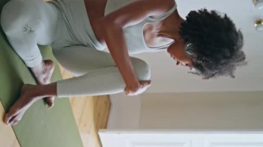Pencere odasında bacaklarını açan zayıf bir kız. Kulaklıklı kadın tablet yoga dersini seyrediyor. Halıya dikey olarak meditasyon yapıyor. Afrikalı sakin kadın vücudu ısıtıyor. Kıvırcık saç modeli evde egzersiz yapıyor..