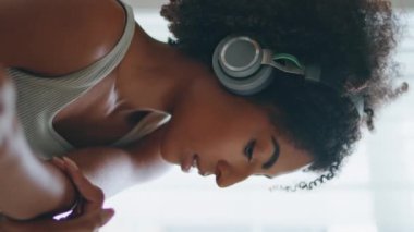 Ev portresi çekilirken odaklanmış kadın ellerini ısıtıyor. Slim Afrikalı Amerikalı kadın, kulaklık takıp müzik dinliyor ve sabah egzersizlerini dikey olarak videoya çekiyor. Formda kız kollarını uzatıyor ve kameraya yakın çekim yapıyor.
