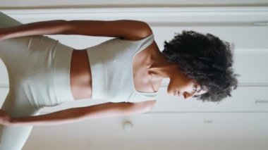 Sakin model evde yoga yapıyor. Afro-Amerikan rahat kız, Asana 'ya dikey beyaz mekanda poz veriyor. Sıska sporcu kadın yatak odasında vücut germe egzersizi yapıyor. Spor konsepti