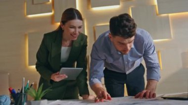 İnşaat uzmanları mühendislik ajansında mimari proje oluşturuyorlar. İki profesyonel mimar şirket ofisindeki bina planında çalışıyor. Tabletteki adama teknolojik verileri gösteren kadın.