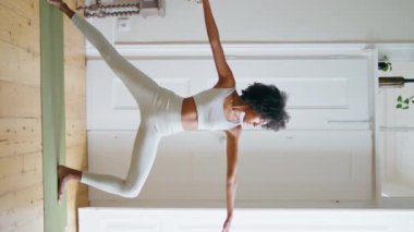 Evde yoga yapan sakin bir bayan. Afro-Amerikan rahat kız halının üzerinde dikey poz veriyor. Beyaz iç kısımda zayıf sporcu kadın uzanıyor. Spor eğitmeni Asana 'nın yan açısını genişletiyor..