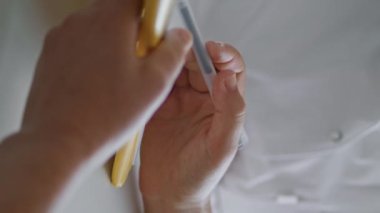 Kadın elleri elinde kalemle kozmetikçiye dokümanlarda ayrıntıları gösteriyor. Bornozla dikey yakın plan çekimde. Bilinmeyen bir bayan müşteri, tıbbi uzmanla ameliyat hakkında kağıt anlaşması okuyor.