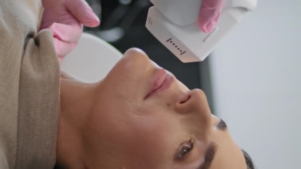 在美容院接受超声治疗的妇女垂直天使特写 做超声治疗的美容师面对皮肤 美容师在现代门诊部进行非手术整容 — 图库视频影像