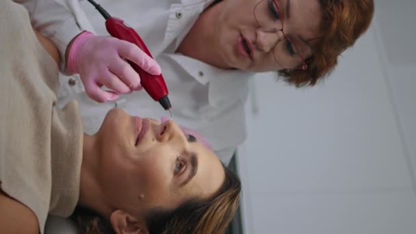 五金专业的面部治疗制造认证皮肤科医生在美容院垂直拍摄特写 医生切除妇女的皮肤瑕疵 美容师在器械上作塑化处理 — 图库视频影像
