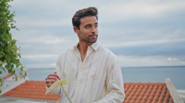 Romantik adam bulutlu gökyüzü arkaplanına yakından bakıyor. Latin yetişkin, maço, yaz şehir manzarasında elinde çiçekle bekleyen kız arkadaş. Dışarıda tek başına duran yakışıklı, tıraşsız adam. İnsan yaşam tarzı 