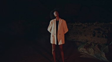 Beyaz ceketli şık bir model kumsalda poz veriyor. Karanlık kayalıklarda gümüş renkli parti makyajlı seksi bayan. Çekici Afro-Amerikan Gece Kayalıkları 'ndaki kamera. Dışarıdaki şenlikli bayan..