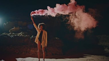 Gece gösterisinde sis bombasını kutlayan kadın. Festivalde elinde pembe gaz bombası tutan seksi kız. Projektör ışığında poz veren güzel Afro-Amerikan. Moda modeli.