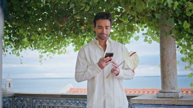 Şehir manzarası gününde elinde çiçekle mesajlar tutan mutlu bir beyefendi. Gülümseyen yakışıklı adam deniz manzaralı balkonda sosyal medya sohbeti yapan kız arkadaş bekliyor. Tıraşsız esmer yeşil ağacın altında dinleniyor.