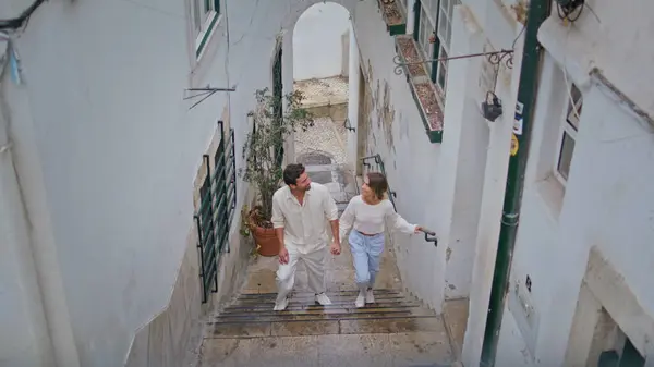 Romantic couple walking stairs up at tiny street. Handsome brunette gentleman talking smiling girlfriend at old town. Relaxed happy pair enjoying anniversary date strolling summer mediterranean city